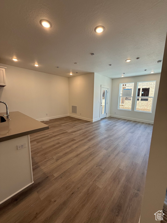 Unfurnished living room featuring dark wood finished floors, baseboards, recessed lighting, a textured ceiling, and a sink
