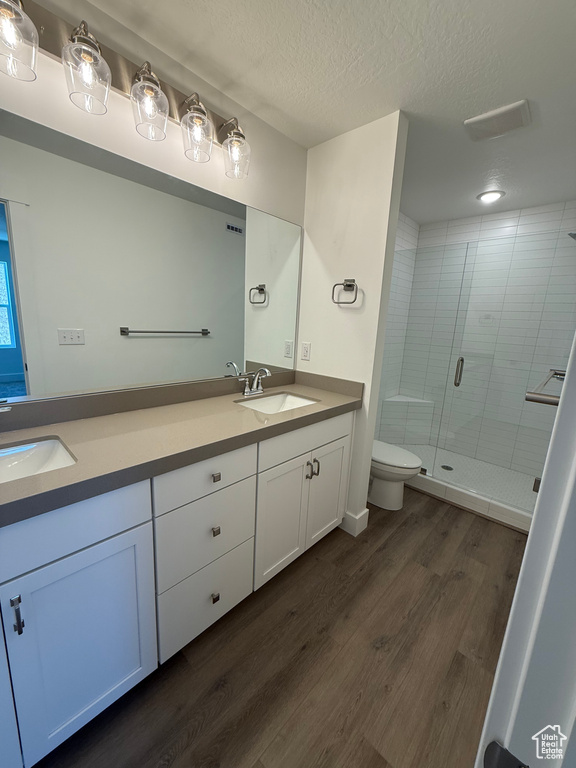 Full bath with double vanity, wood finished floors, a stall shower, toilet, and a textured ceiling