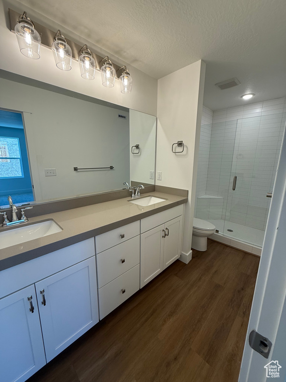 Full bathroom with double vanity, a shower stall, wood finished floors, toilet, and a textured ceiling