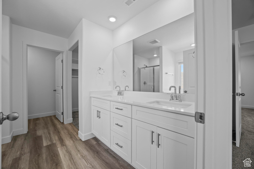 Bathroom featuring a shower stall, double vanity, wood finished floors, a spacious closet, and baseboards