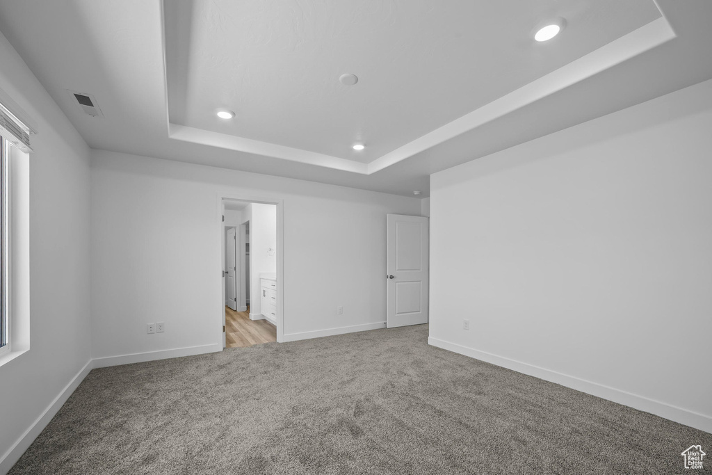 Unfurnished bedroom featuring a tray ceiling, light colored carpet, recessed lighting, and baseboards