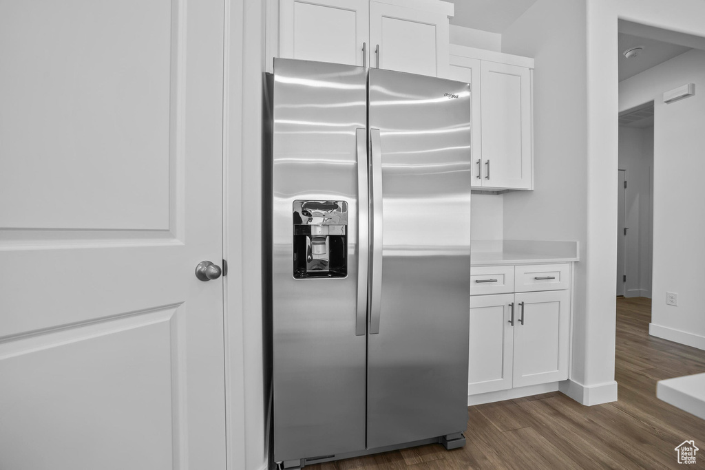 Kitchen with stainless steel fridge, white cabinetry, dark wood-style flooring, light countertops, and baseboards