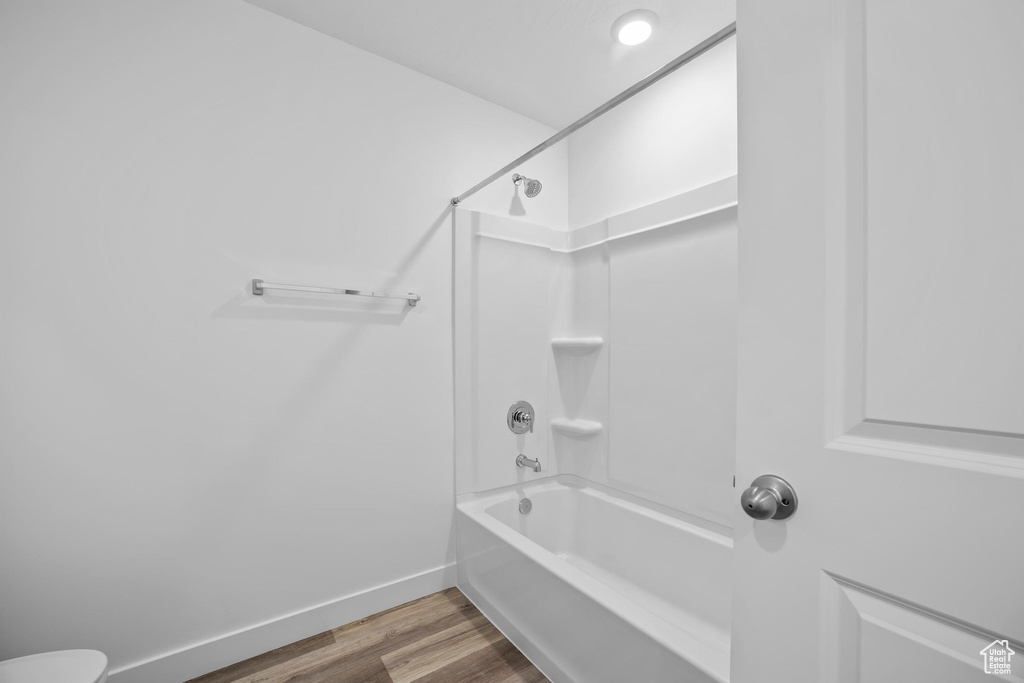 Bathroom featuring wood finished floors, tub / shower combination, baseboards, and toilet