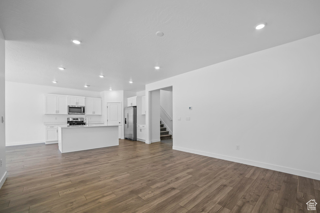 Unfurnished living room featuring stairs, recessed lighting, dark wood-type flooring, and baseboards