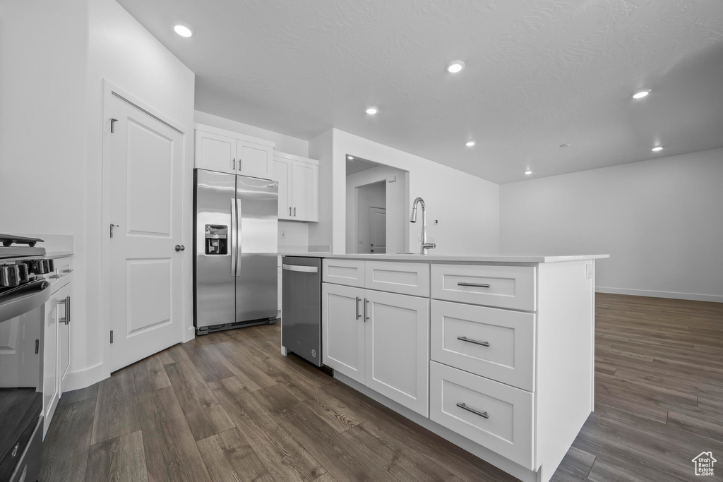 Kitchen with appliances with stainless steel finishes, dark wood finished floors, white cabinets, an island with sink, and recessed lighting