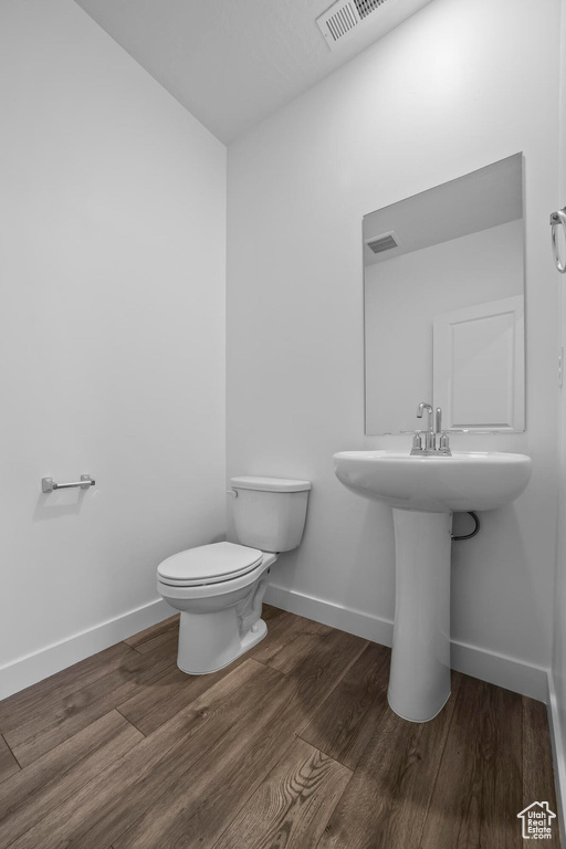 Half bathroom with toilet, baseboards, wood finished floors, and a sink