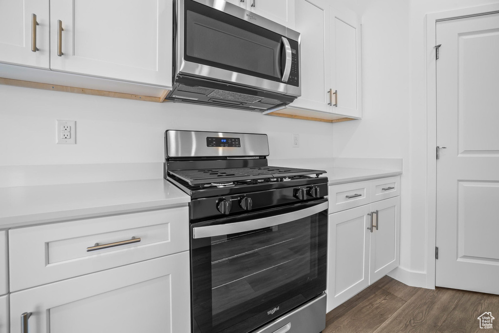 Kitchen with appliances with stainless steel finishes, white cabinets, light countertops, and dark wood finished floors