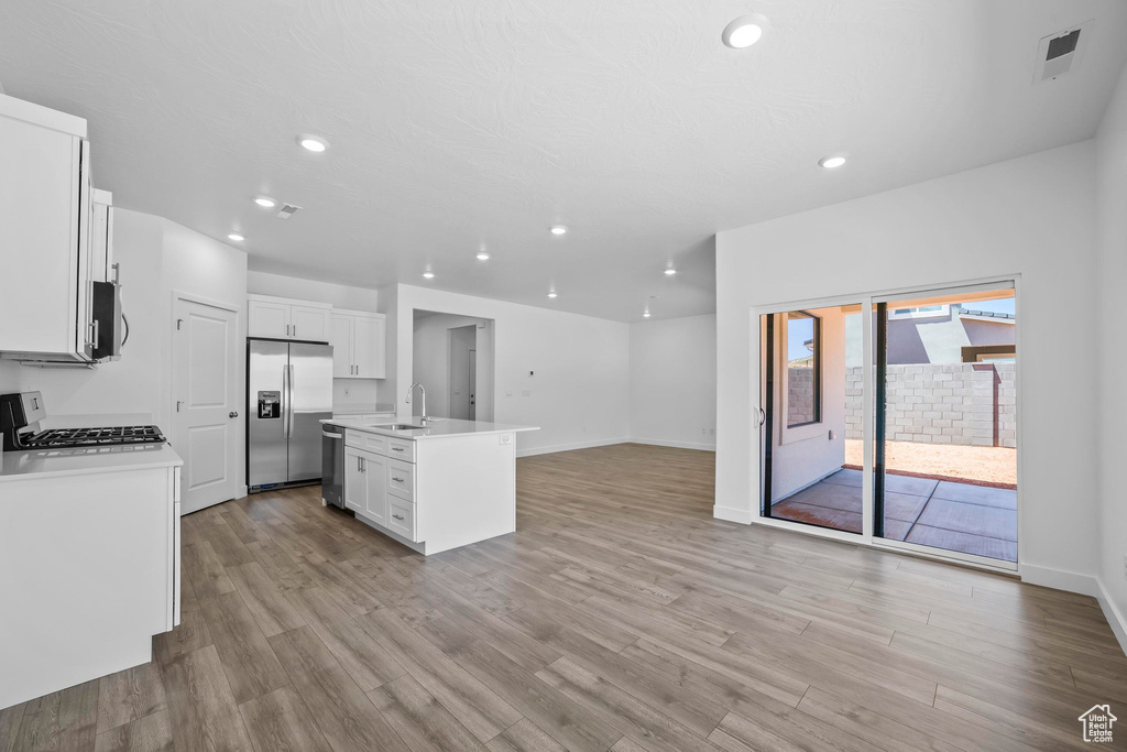 Kitchen featuring appliances with stainless steel finishes, a sink, open floor plan, light wood finished floors, and recessed lighting