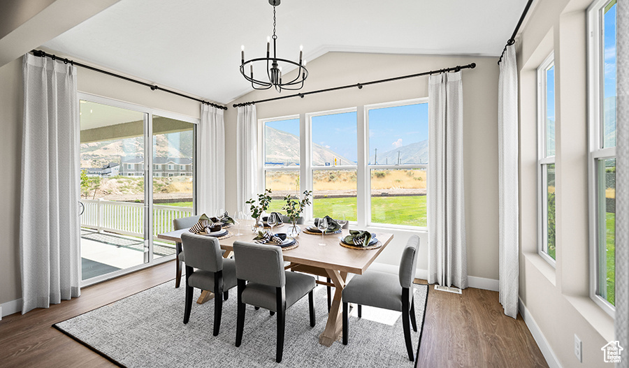 Dining space with vaulted ceiling, plenty of natural light, a chandelier, and wood finished floors