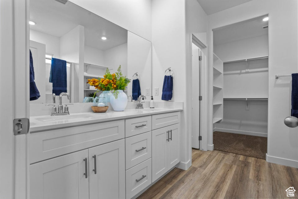 Full bath with double vanity, wood finished floors, a walk in closet, and recessed lighting