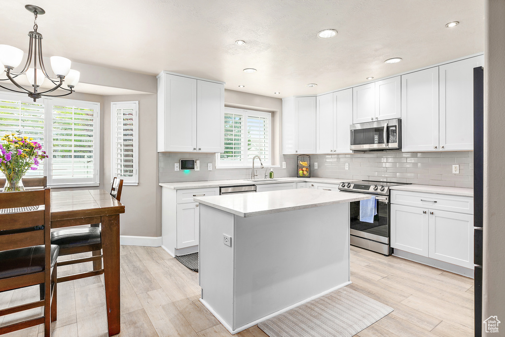 Kitchen featuring appliances with stainless steel finishes, a chandelier, light wood-type flooring, light countertops, and decorative backsplash
