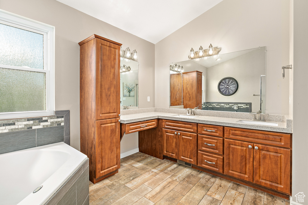 Full bath with plenty of natural light, double vanity, a bath, lofted ceiling, and wood finished floors