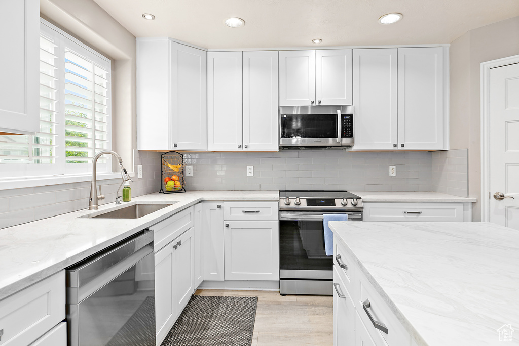 Kitchen featuring stainless steel appliances, a sink, light stone counters, white cabinets, and recessed lighting