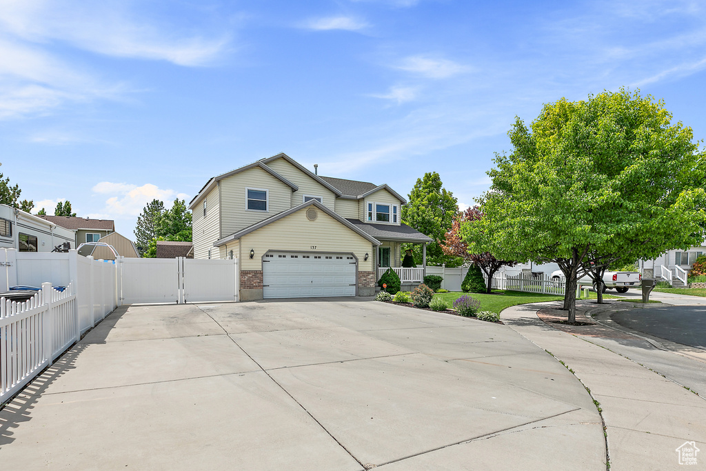 View of front facade with driveway, a garage, brick siding, and a gate