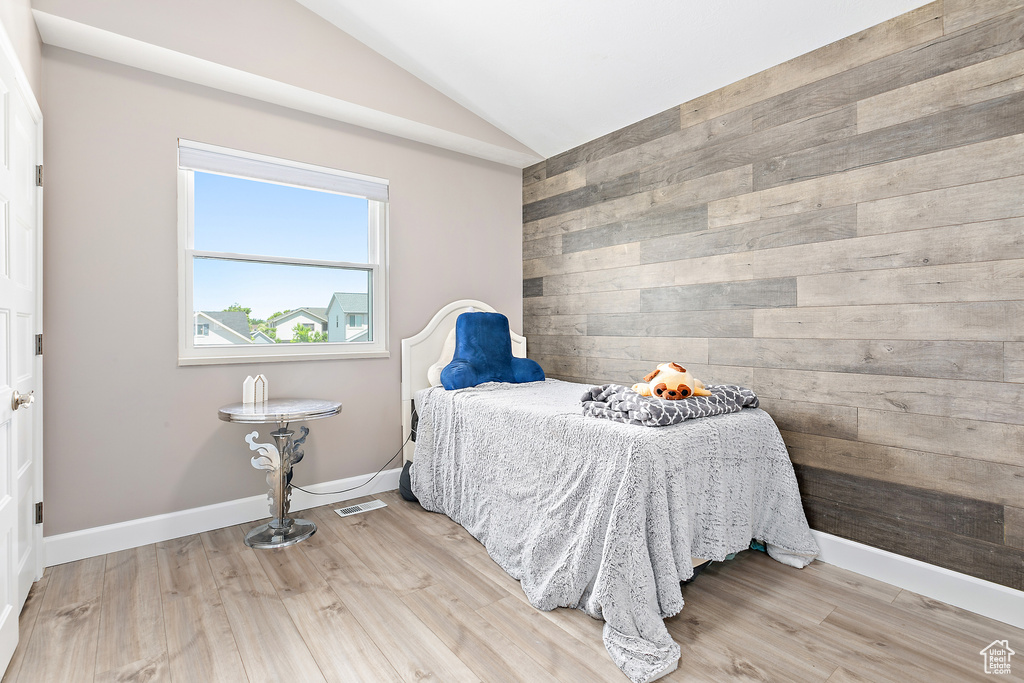 Bedroom with lofted ceiling, wooden walls, light wood-type flooring, and baseboards