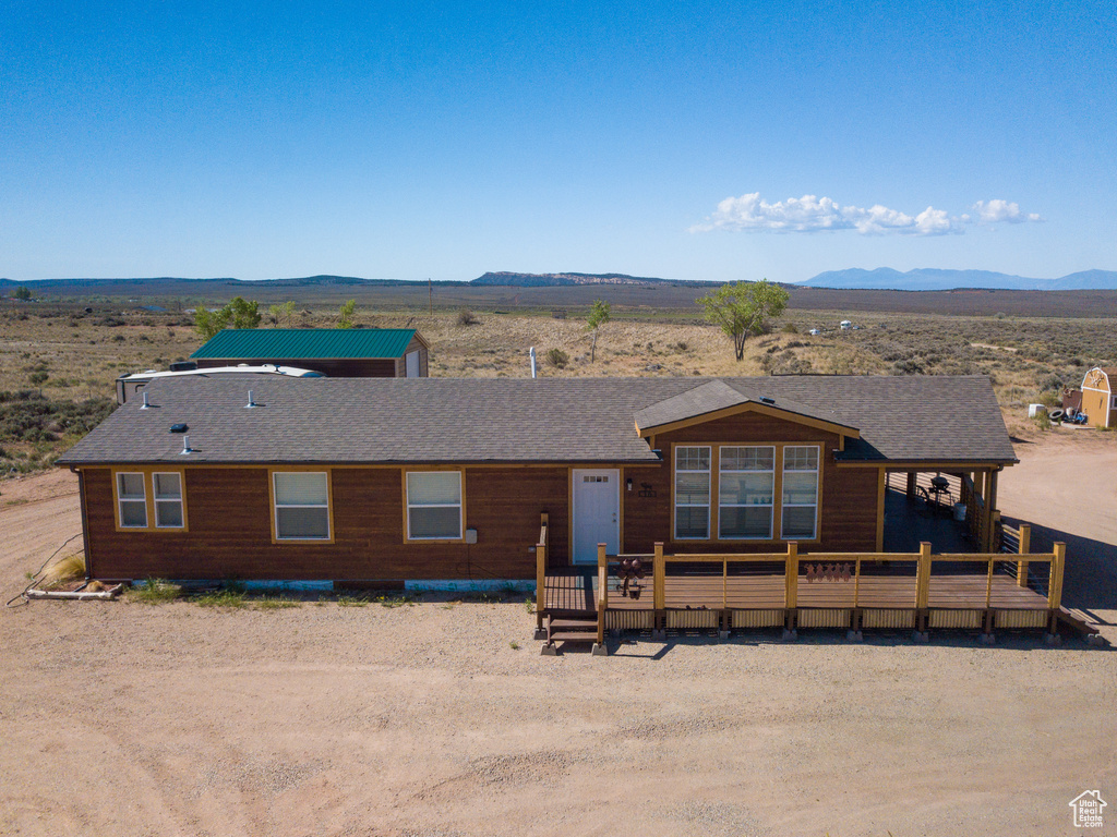 View of front of property with a deck with mountain view, view of desert, and roof with shingles