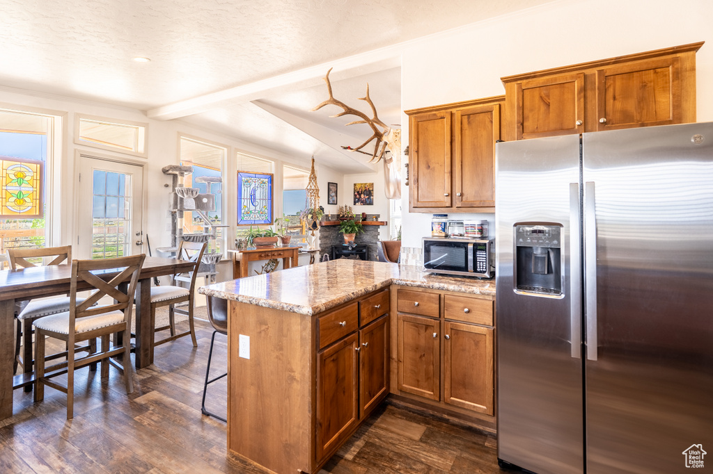 Kitchen with appliances with stainless steel finishes, brown cabinets, a peninsula, and dark wood-style flooring