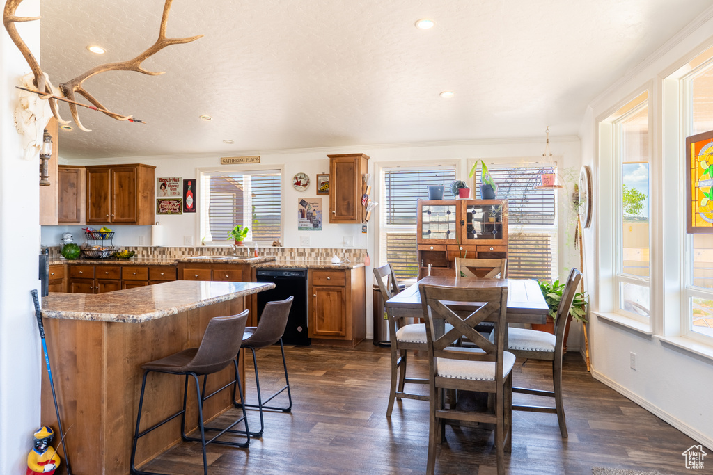 Kitchen featuring black dishwasher, brown cabinetry, dark wood-style floors, a kitchen bar, and recessed lighting