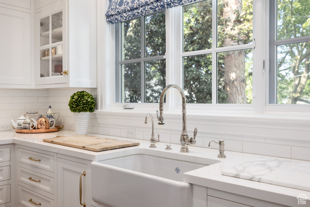 Kitchen featuring a sink, white cabinets, glass insert cabinets, tasteful backsplash, and healthy amount of natural light
