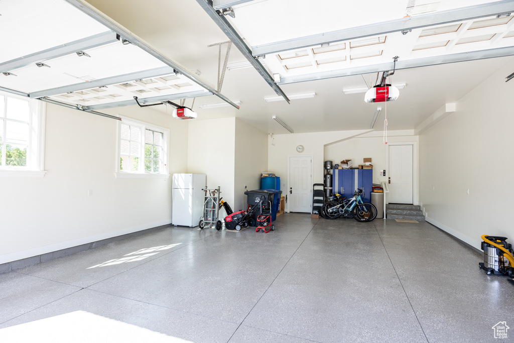Garage with a garage door opener, freestanding refrigerator, and baseboards