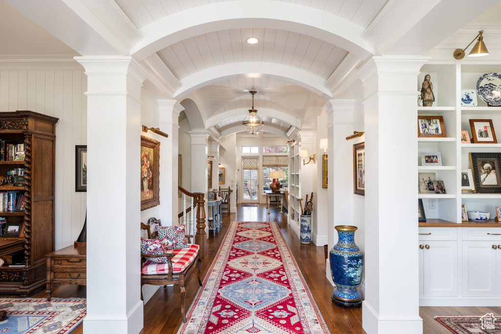 Hallway with ornate columns, wood finished floors, arched walkways, lofted ceiling, and built in shelves