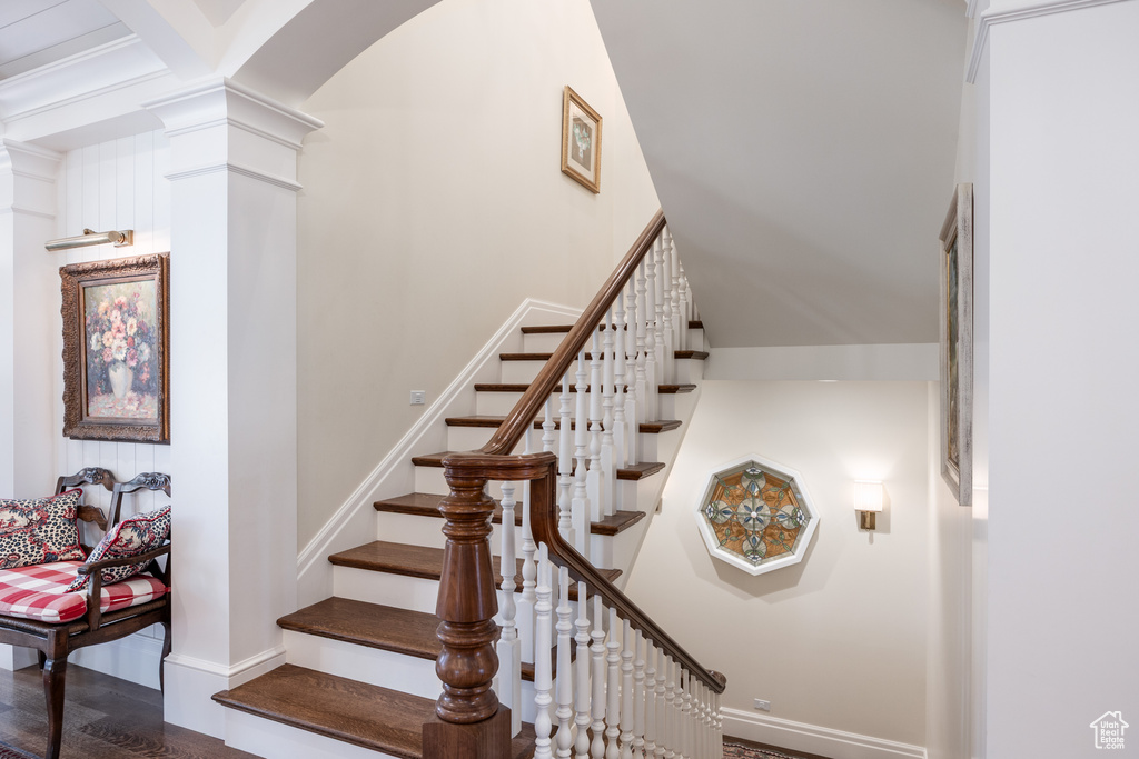 Staircase featuring decorative columns, baseboards, arched walkways, and wood finished floors