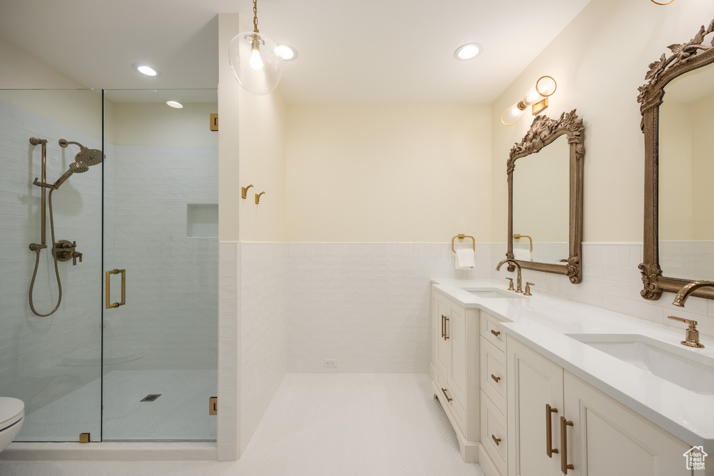 Bathroom featuring a stall shower, double vanity, toilet, recessed lighting, and a wainscoted wall