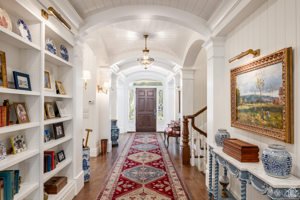 Foyer with arched walkways, dark wood finished floors, vaulted ceiling, and decorative columns