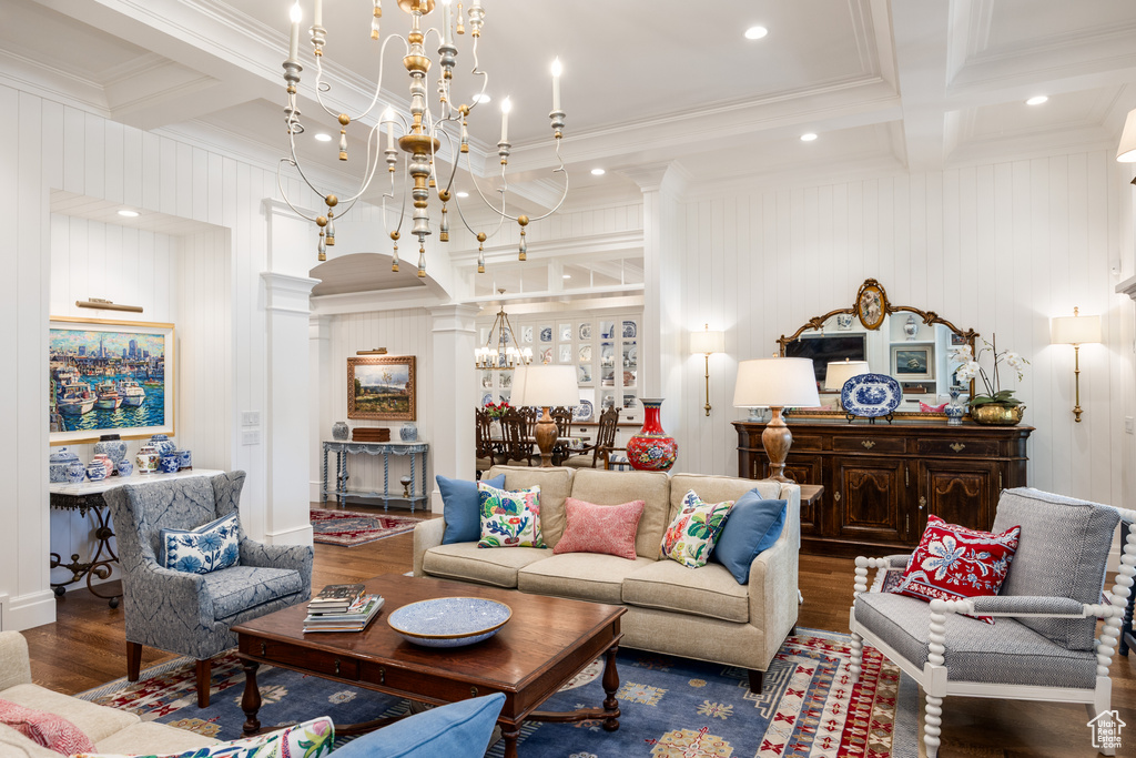 Living area with a chandelier, beam ceiling, wood finished floors, ornamental molding, and decorative columns
