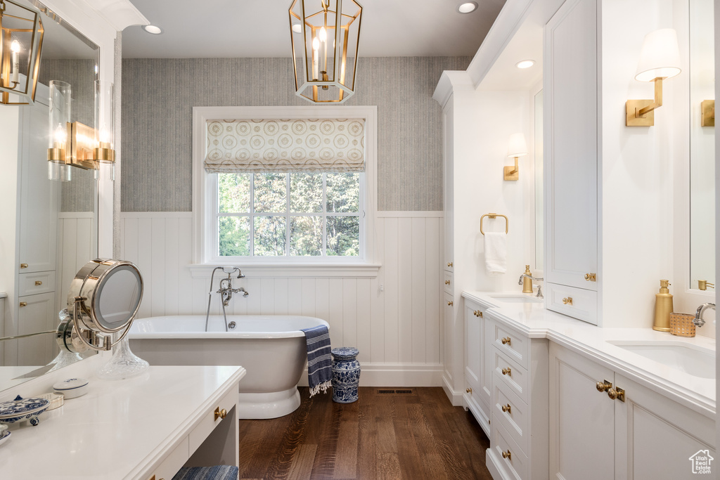 Full bath with wood finished floors, wallpapered walls, wainscoting, double vanity, and a freestanding bath
