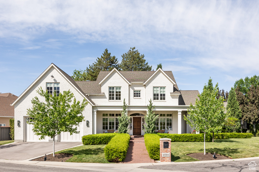 View of front facade featuring brick siding, a front yard, driveway, and a garage