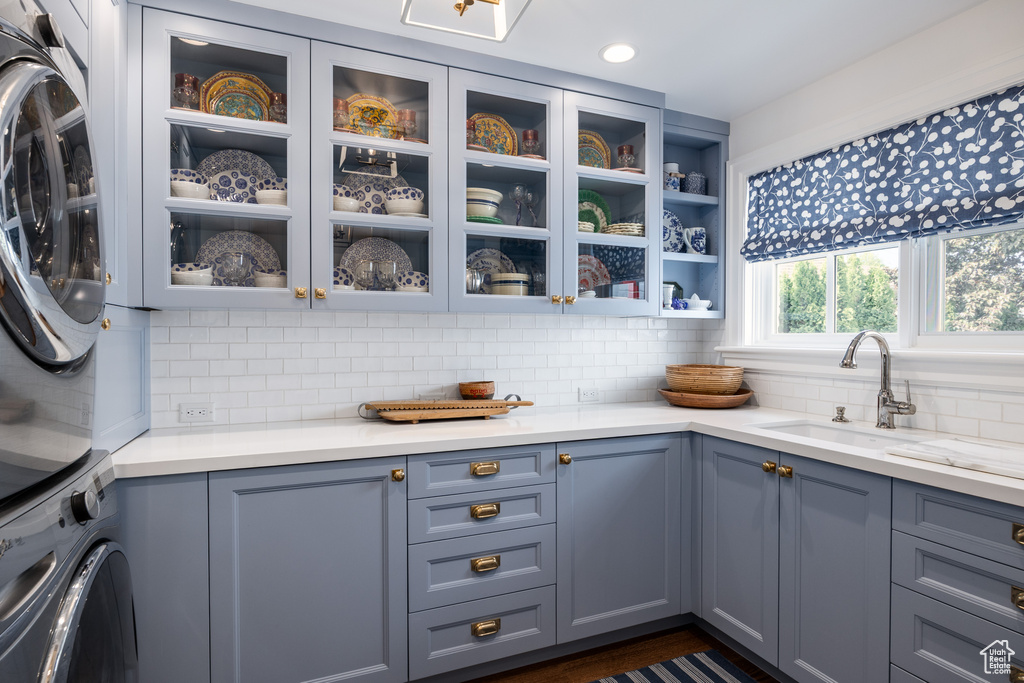 Kitchen featuring stacked washer and clothes dryer, glass insert cabinets, decorative backsplash, recessed lighting, and gray cabinetry