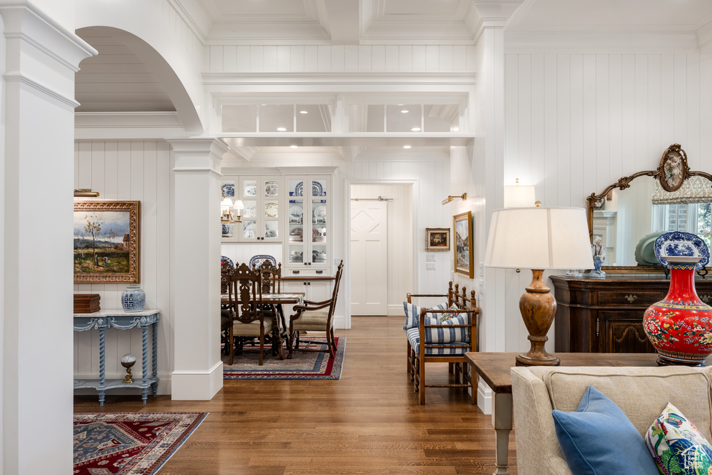 Living room featuring crown molding, wood finished floors, beam ceiling, and decorative columns