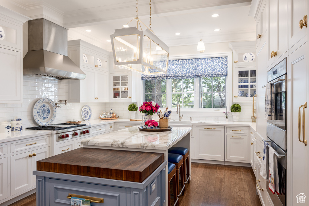 Kitchen featuring butcher block countertops, wall chimney exhaust hood, stainless steel gas stovetop, a chandelier, and a kitchen island