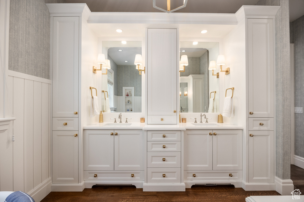 Bathroom featuring double vanity, wood finished floors, wallpapered walls, a decorative wall, and wainscoting