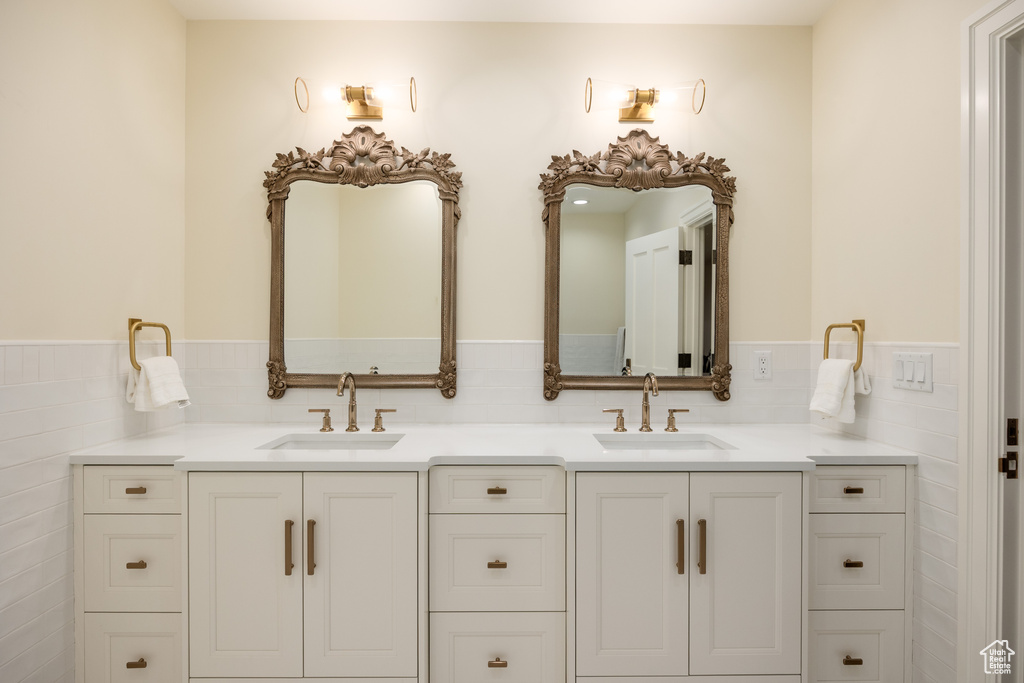 Bathroom with double vanity, a wainscoted wall, and tile walls