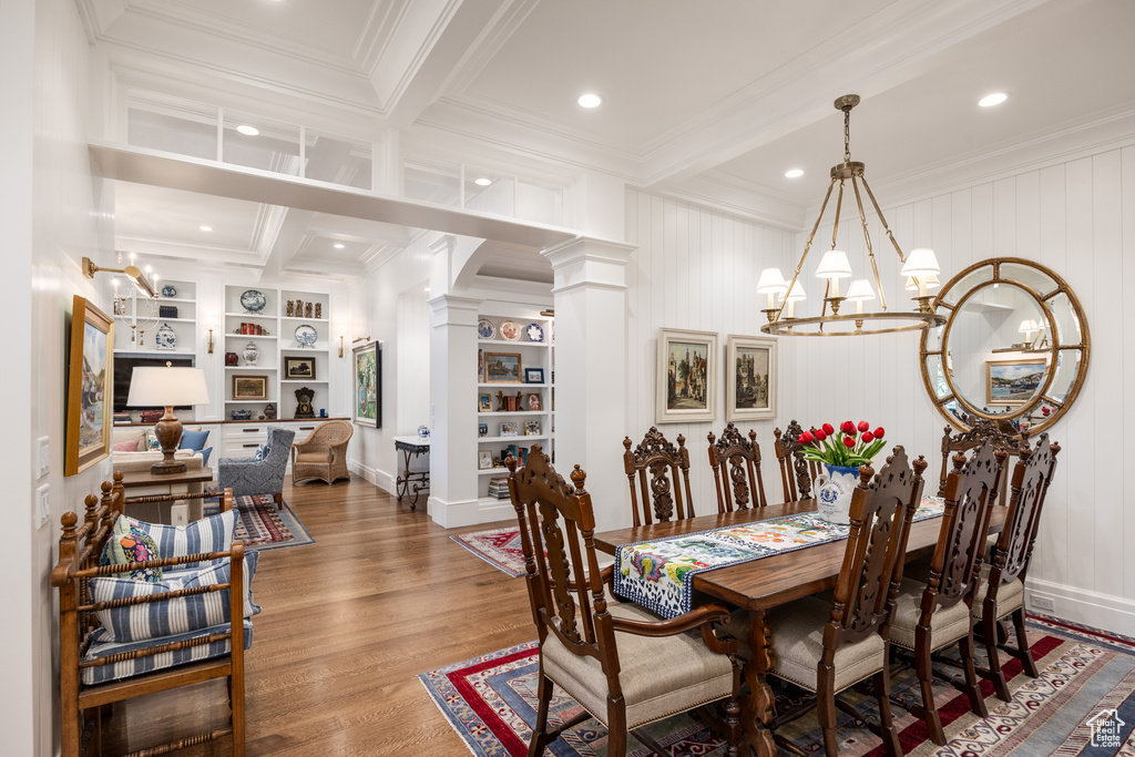 Dining room with decorative columns, ornamental molding, a chandelier, beamed ceiling, and wood finished floors