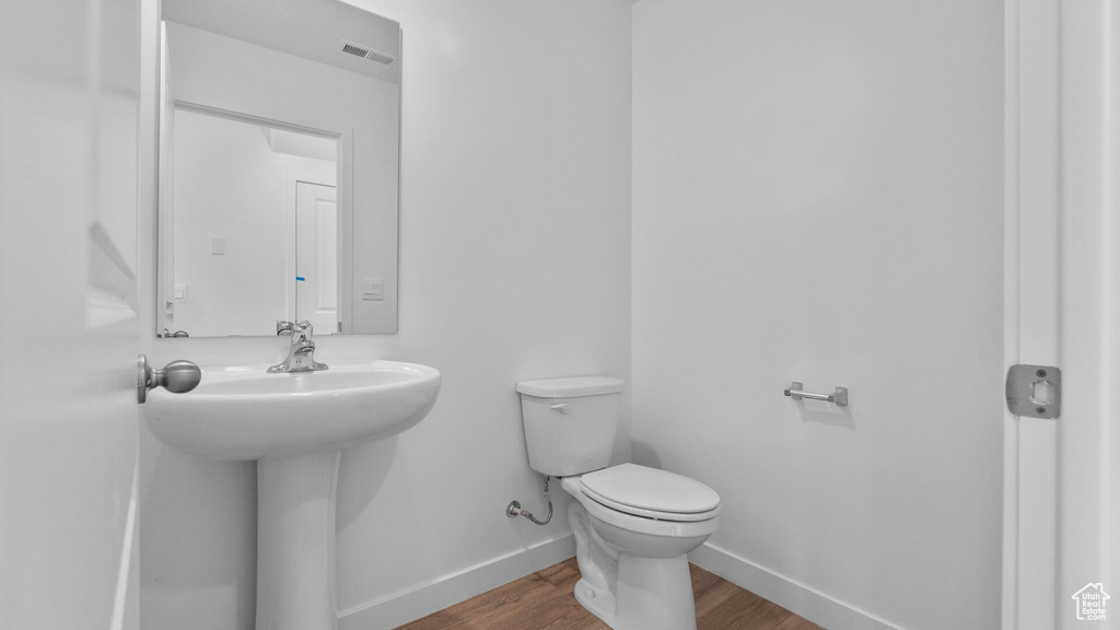 Half bath featuring baseboards, toilet, and wood finished floors