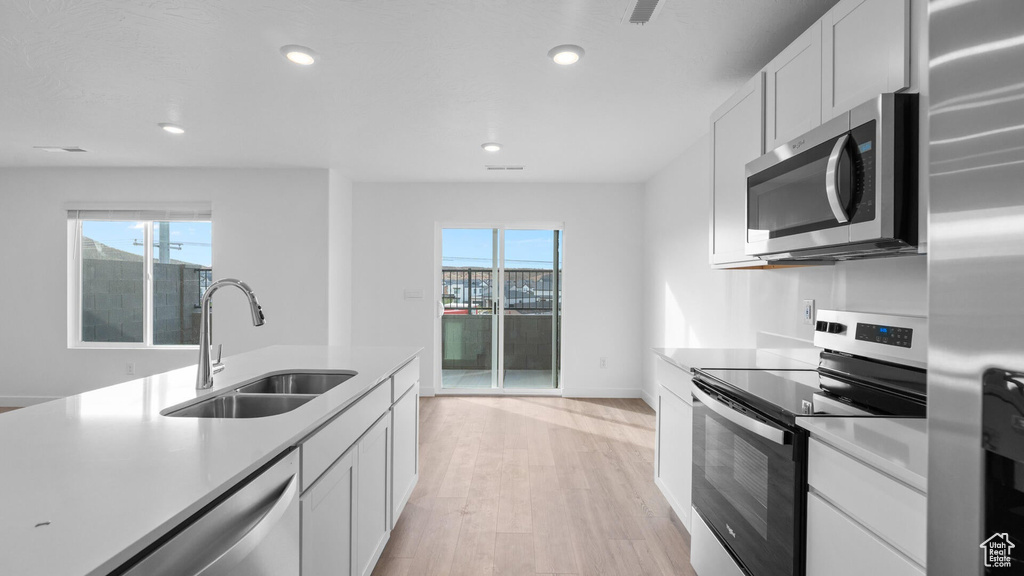 Kitchen with appliances with stainless steel finishes, a sink, light countertops, light wood-type flooring, and white cabinets