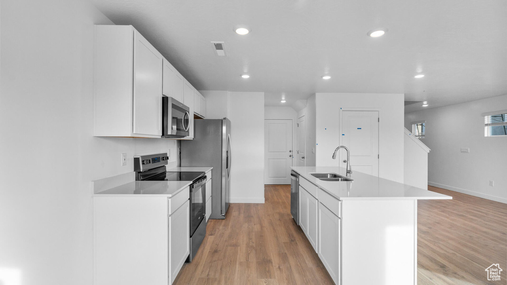 Kitchen with appliances with stainless steel finishes, a sink, white cabinets, baseboards, and an island with sink