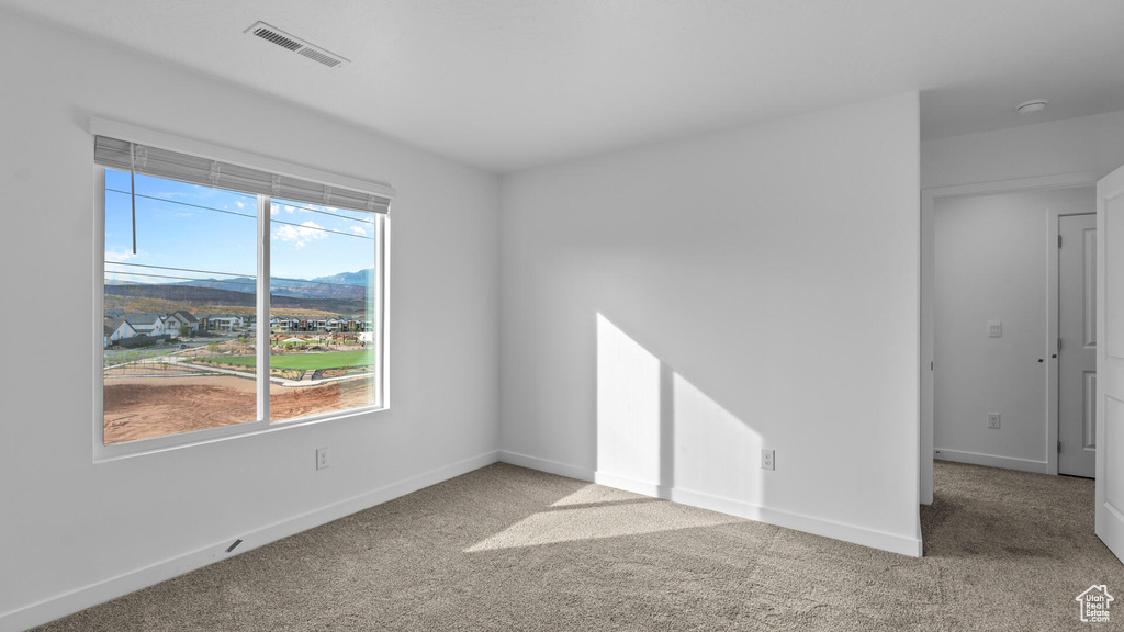 Carpeted spare room with plenty of natural light, baseboards, and a smoke detector