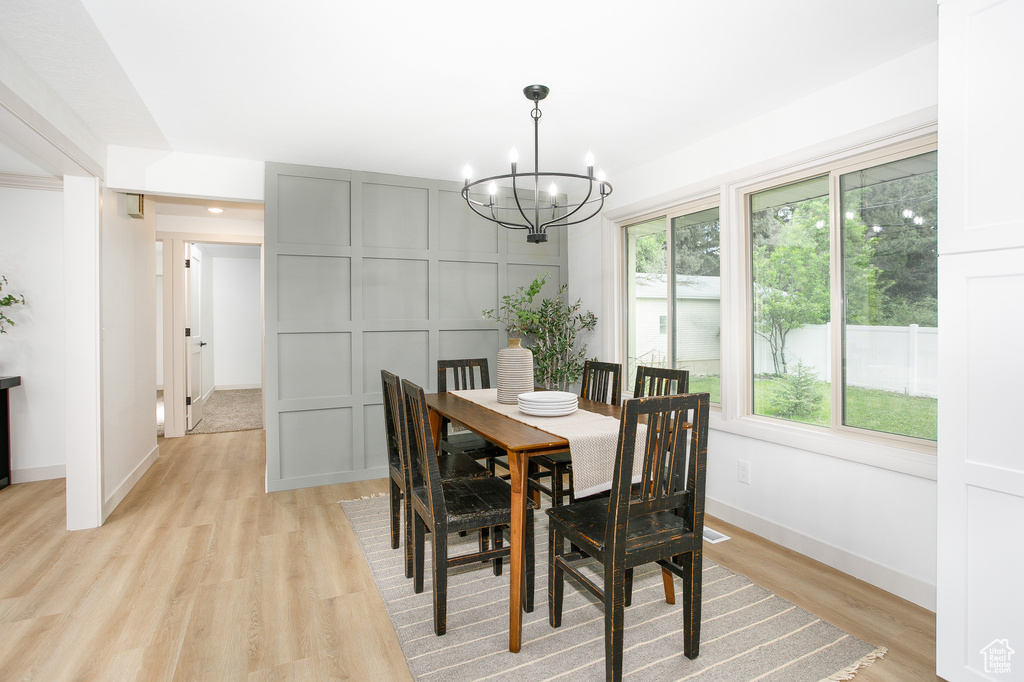 Dining area with a chandelier, light wood-type flooring, baseboards, and a decorative wall