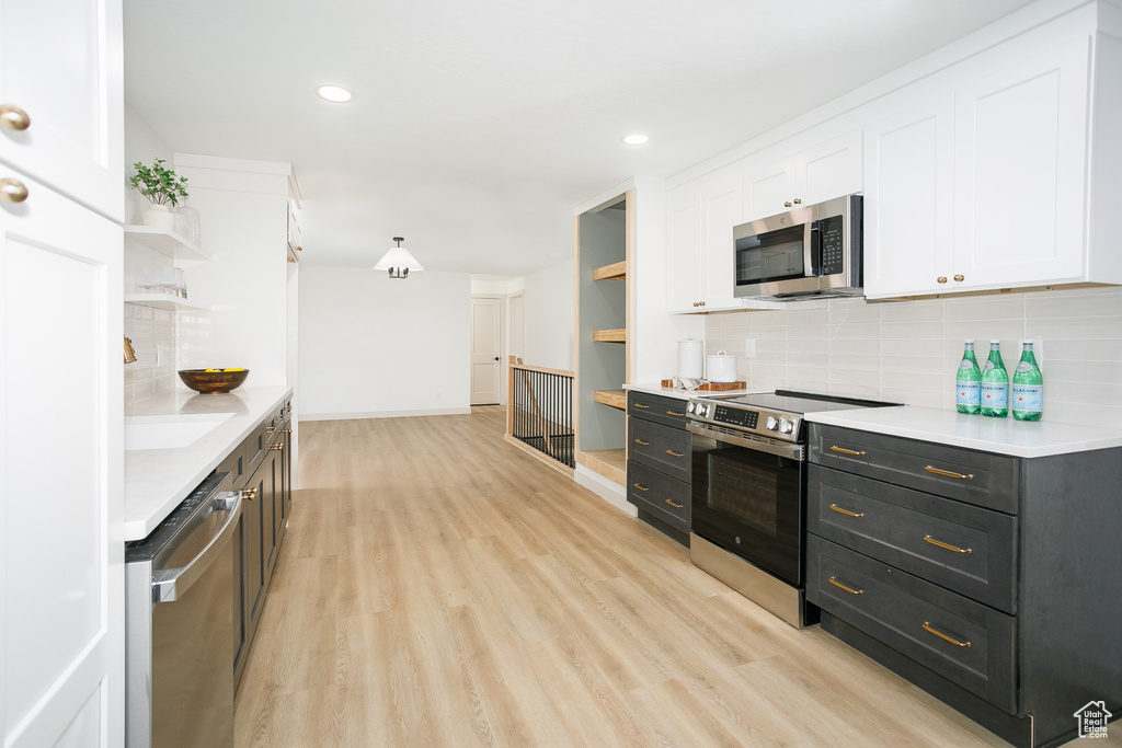 Kitchen featuring open shelves, stainless steel appliances, white cabinets, light wood-type flooring, and tasteful backsplash