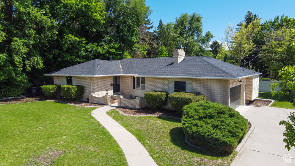 Single story home featuring brick siding, concrete driveway, a garage, roof with shingles, and a front lawn