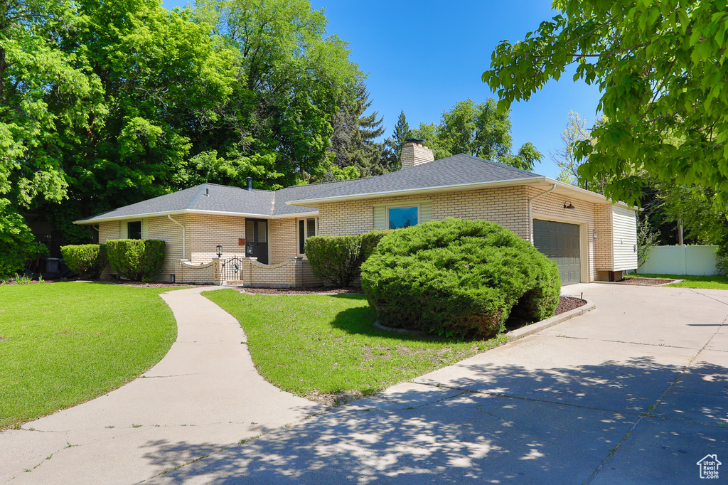 Ranch-style home featuring concrete driveway, an attached garage, brick siding, a chimney, and roof with shingles