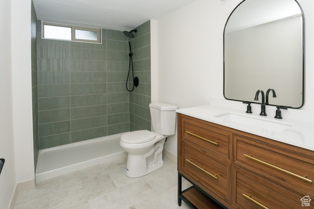 Bathroom featuring vanity, a tile shower, toilet, and baseboards