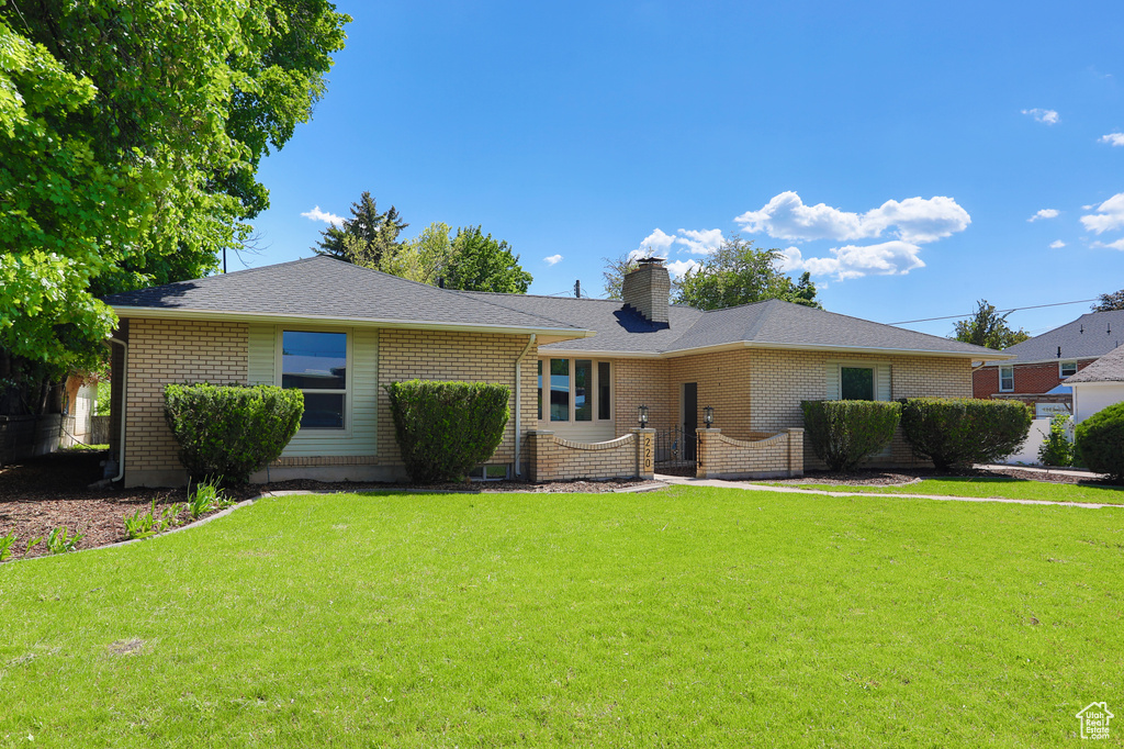 Single story home with a chimney, a front yard, and brick siding