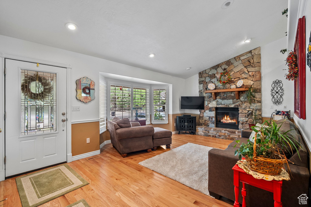 Living area with light wood finished floors, a fireplace, baseboards, vaulted ceiling, and recessed lighting