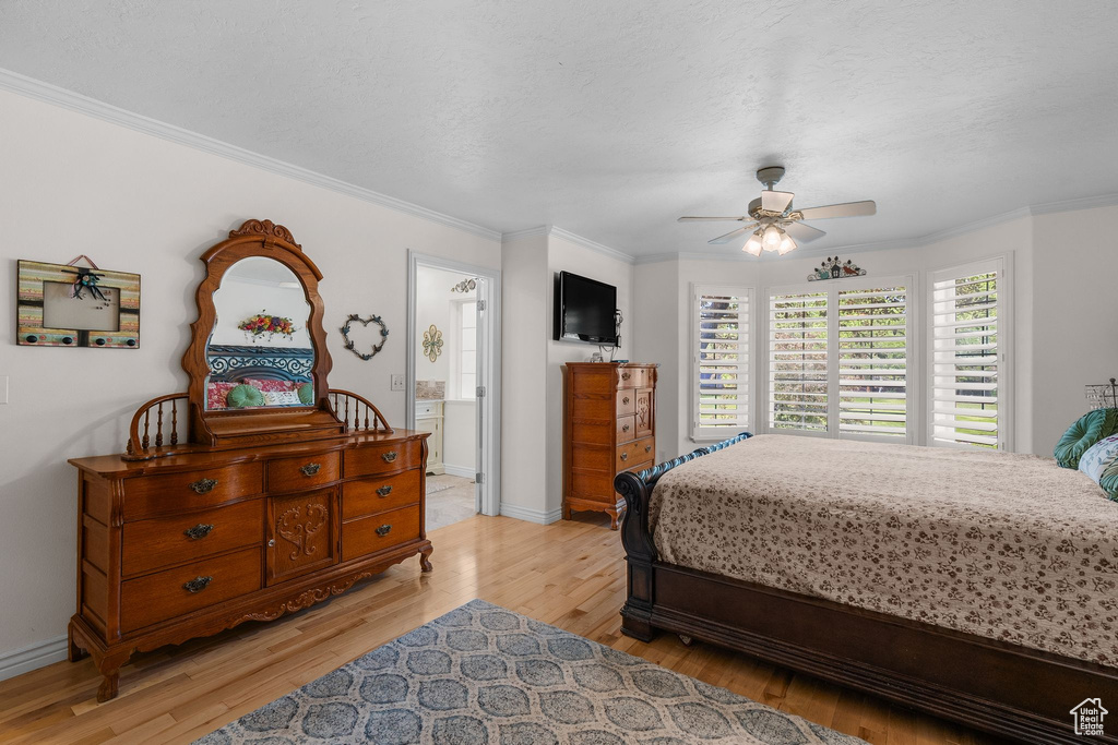 Bedroom featuring light wood-type flooring, ornamental molding, baseboards, a ceiling fan, and a textured ceiling