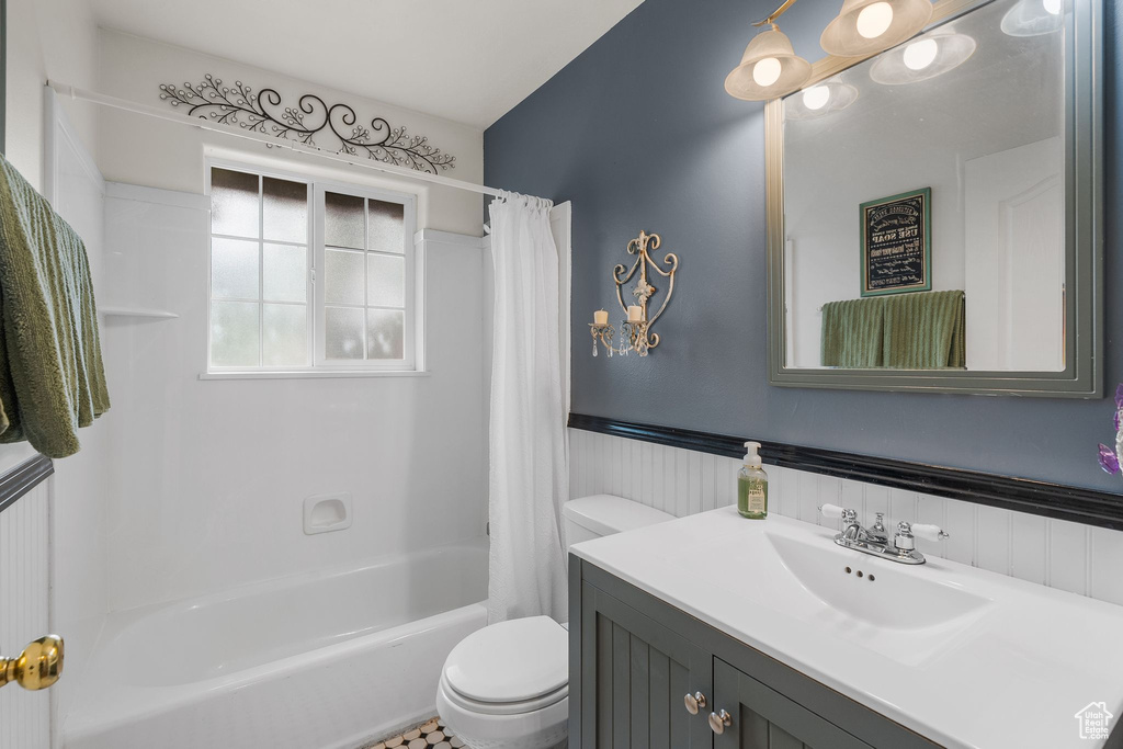 Bathroom featuring toilet, vanity, a wainscoted wall, and shower / tub combo with curtain